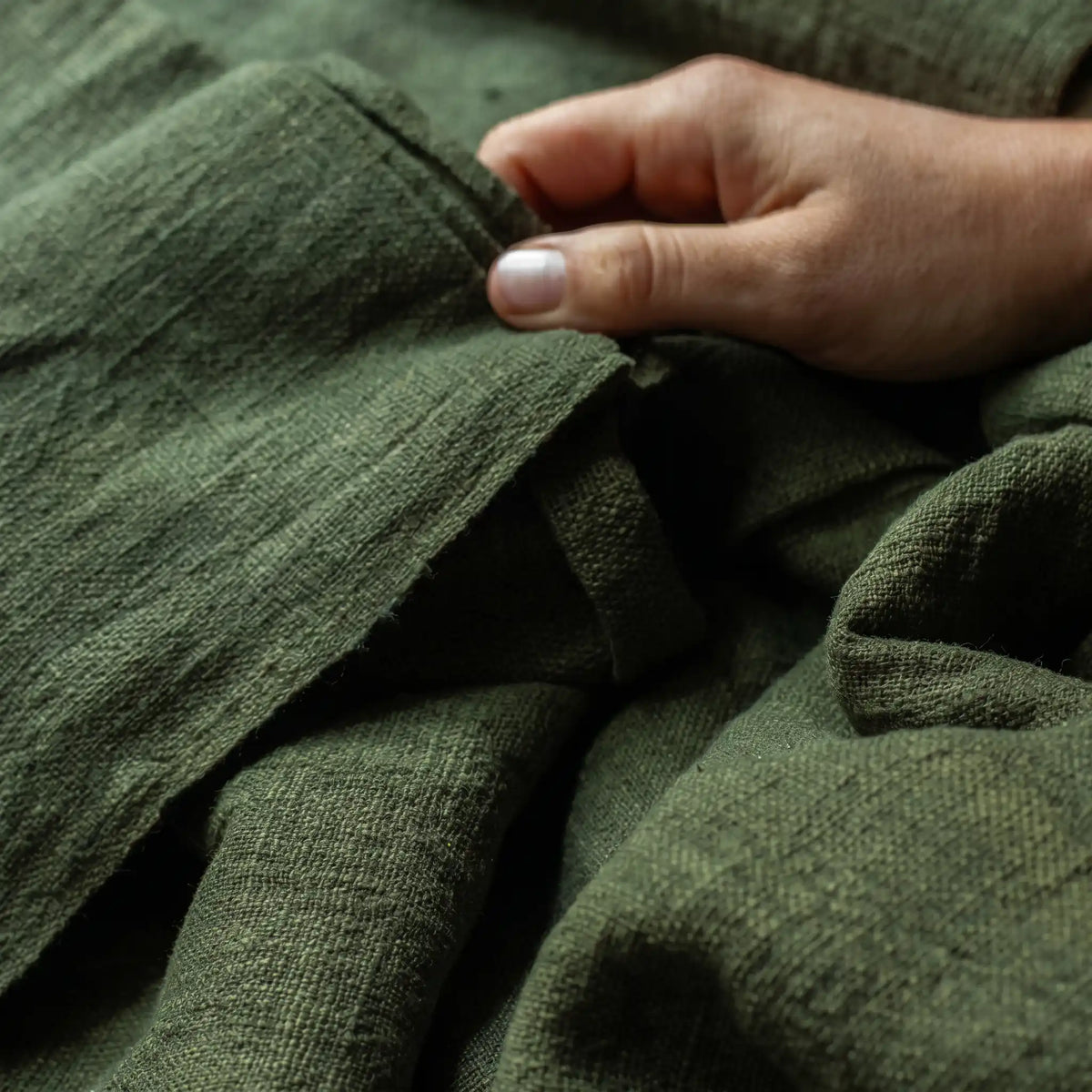 Hand berührt dunkelgrünen Leinenstoff in Nahaufnahme, Material Leinen für leichte und kühlende Sommertextilien