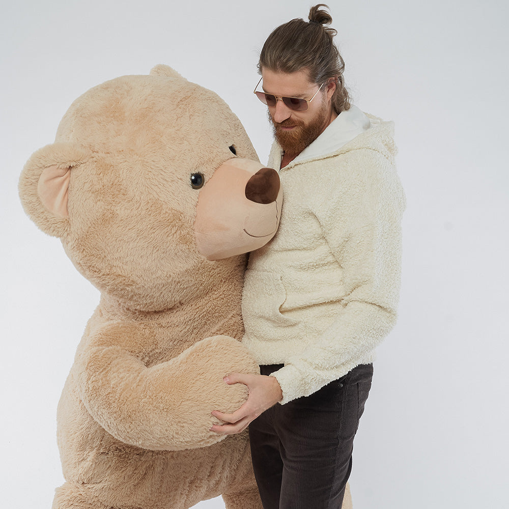 Mann in cremefarbenem Hoodie umarmt einen großen Teddybären, Beispiel für ein persönliches und ungewöhnliches Mitarbeitergeschenk