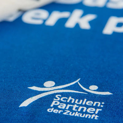 Nahaufnahme eines Siebdrucks auf blauem Textil mit dem Motiv "Schulen: Partner der Zukunft" – Beispiel für langlebigen Siebdruck als Veredelungstechnik.