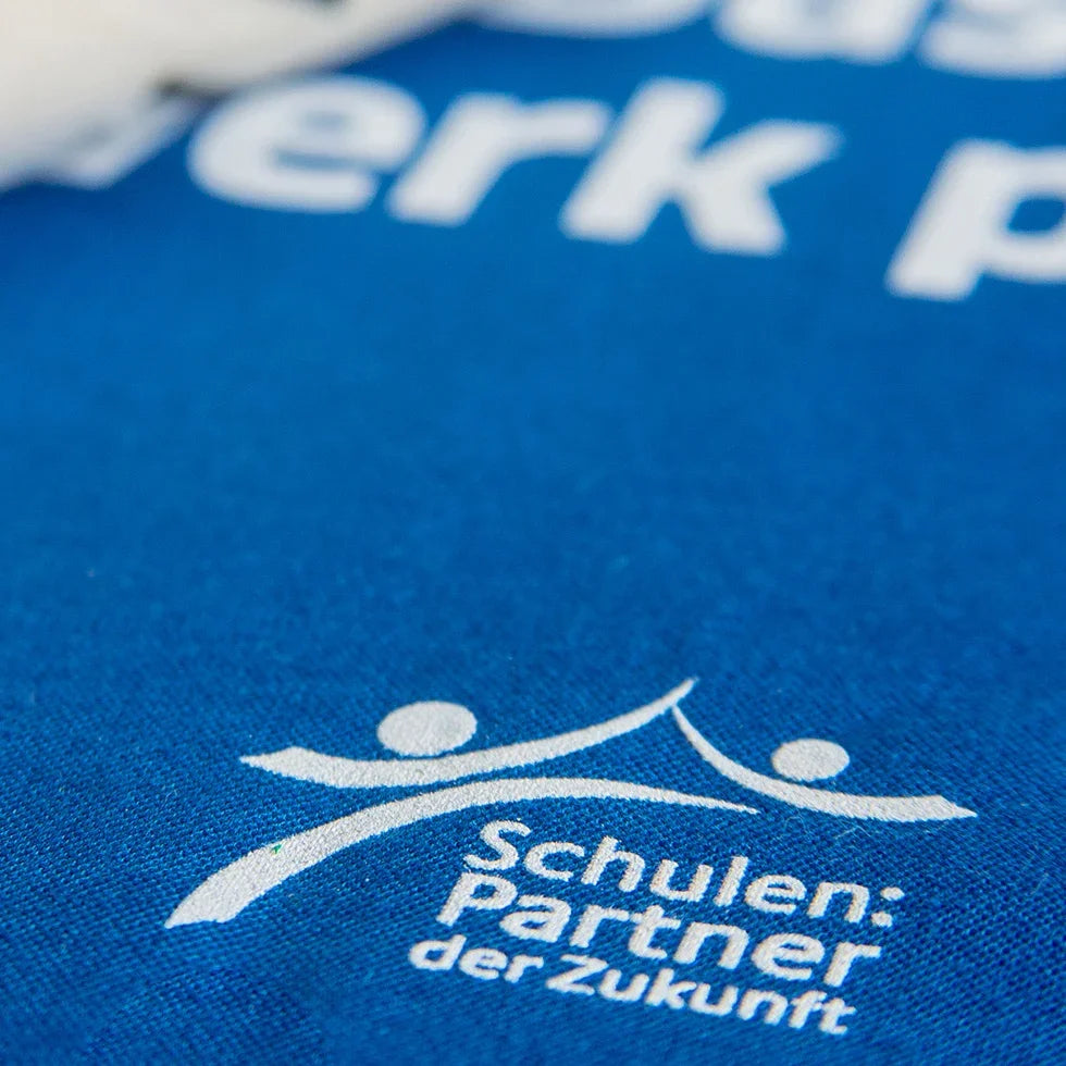 Nahaufnahme eines Siebdrucks auf blauem Textil mit dem Motiv "Schulen: Partner der Zukunft" – Beispiel für langlebigen Siebdruck als Veredelungstechnik.