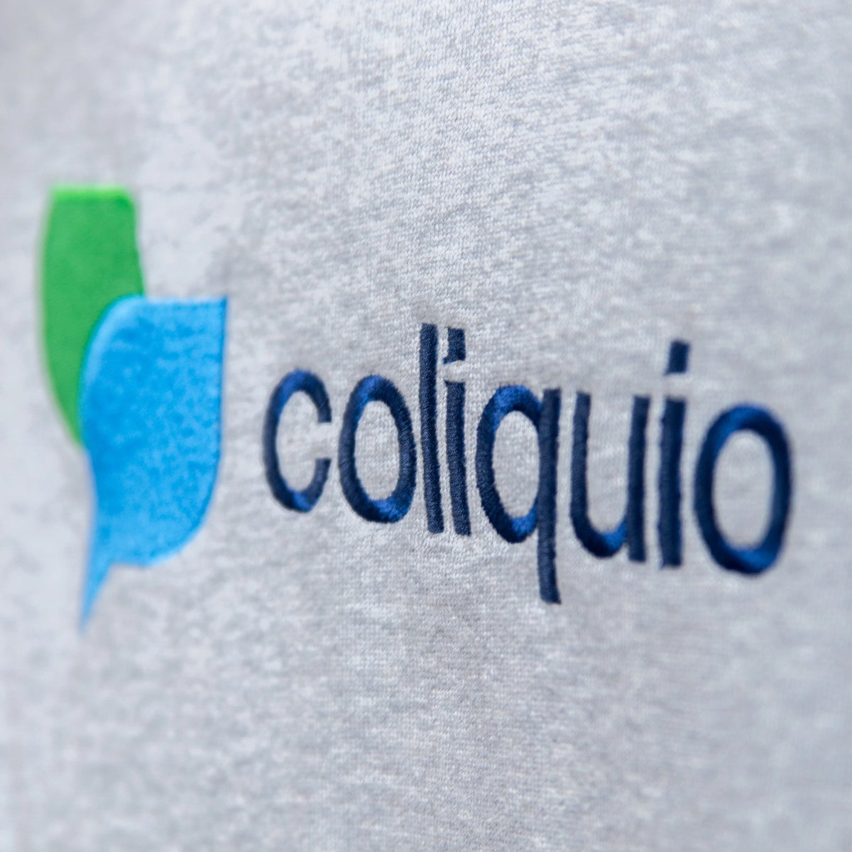 Detailaufnahme einer hochwertigen Logo-Stickerei "coliquio" auf einem grau melierten Sweatshirt, Beispiel für präzise Firmenlogo-Bestickung.