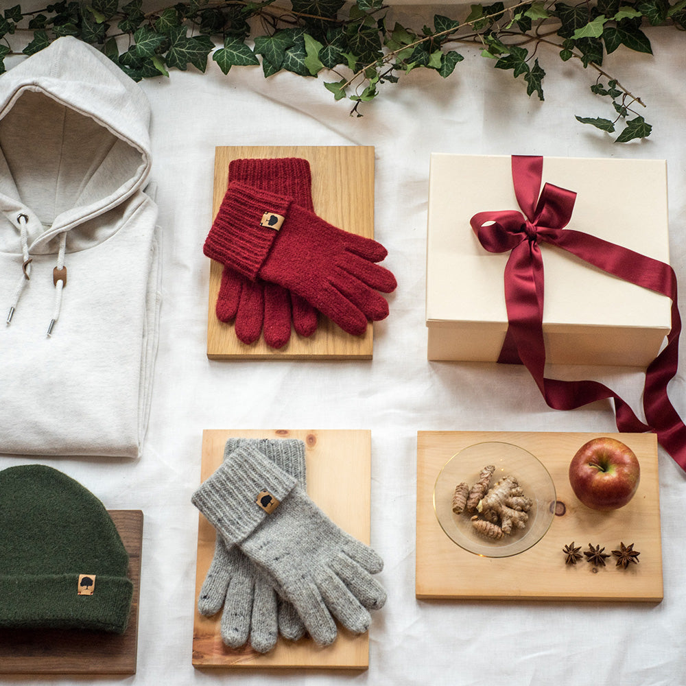 Mütze, Handschuhe und eine mit Schleife verpackte Geschenkbox neben Apfel und Nüssen, winterliches Styling für Weihnachtsgeschenke an Mitarbeiter