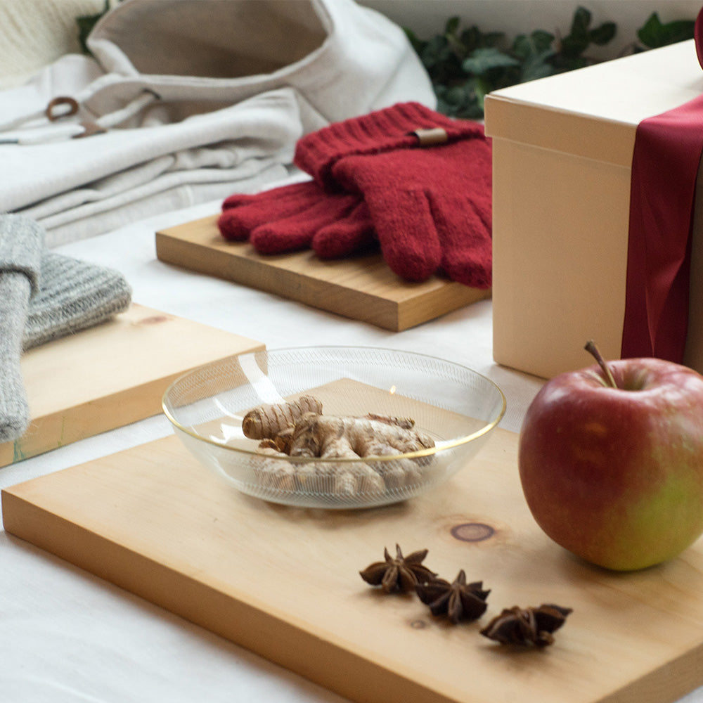 Holzbrett mit roten Handschuhen, Apfel und winterlichen Gewürzen wie Zimt und Sternanis, weihnachtliches Styling für die Geschenke Seite